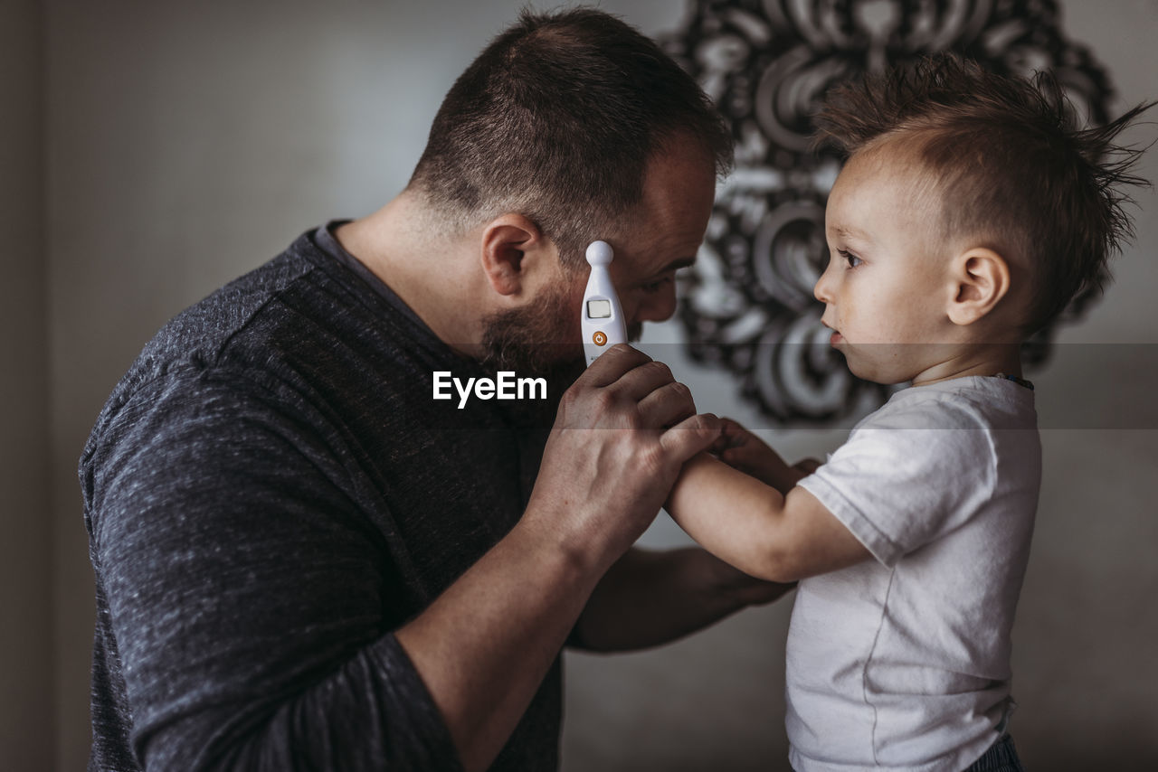 One year old boy taking father’s temperature at home during isolation