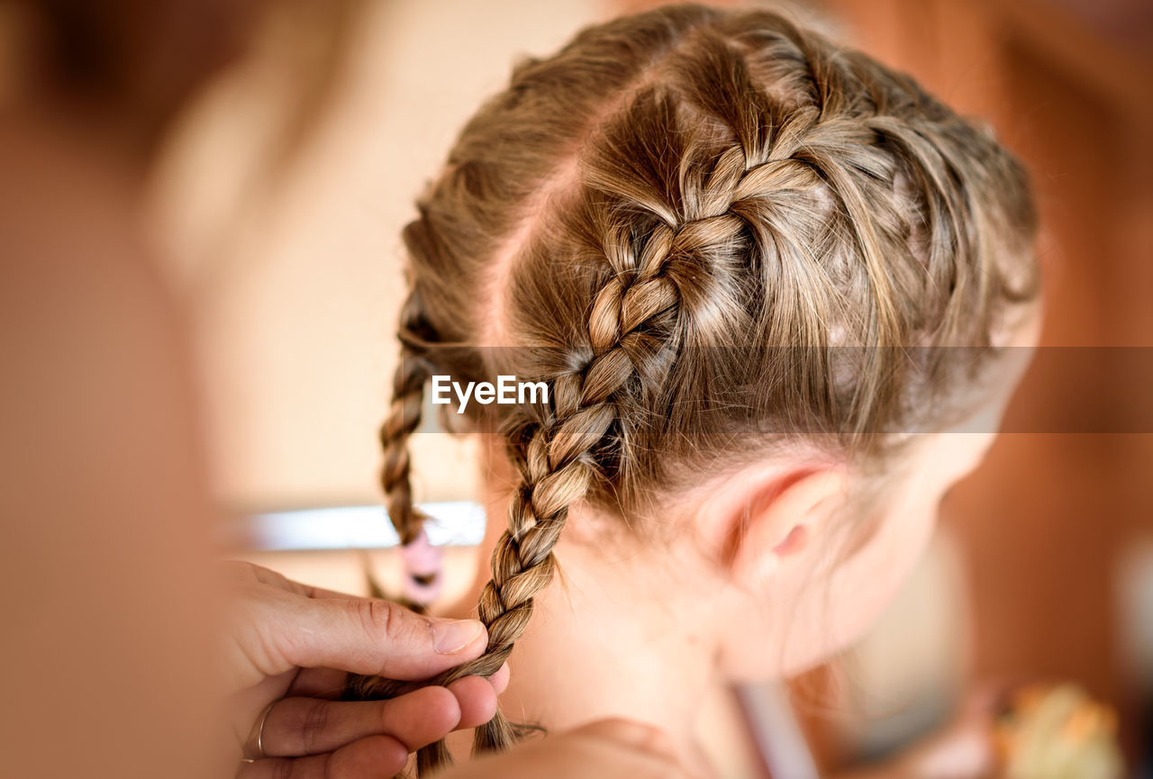 Cropped hands of mother braiding daughter hair