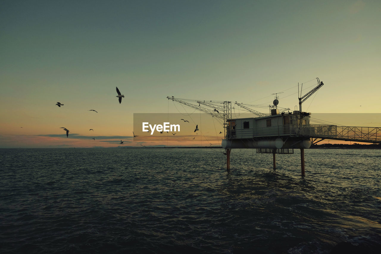 Drilling rig amidst sea against clear sky during sunset