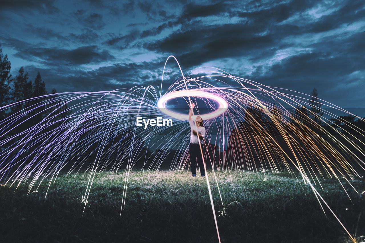 Woman standing amidst wire wool on field against sky