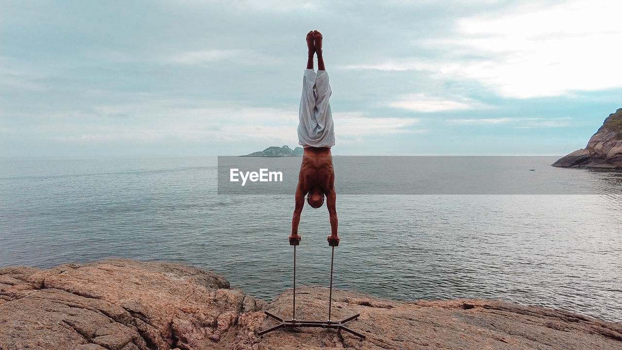 Young adult man doing circus acrobatic handstand upside down on mountain in brazil during day light