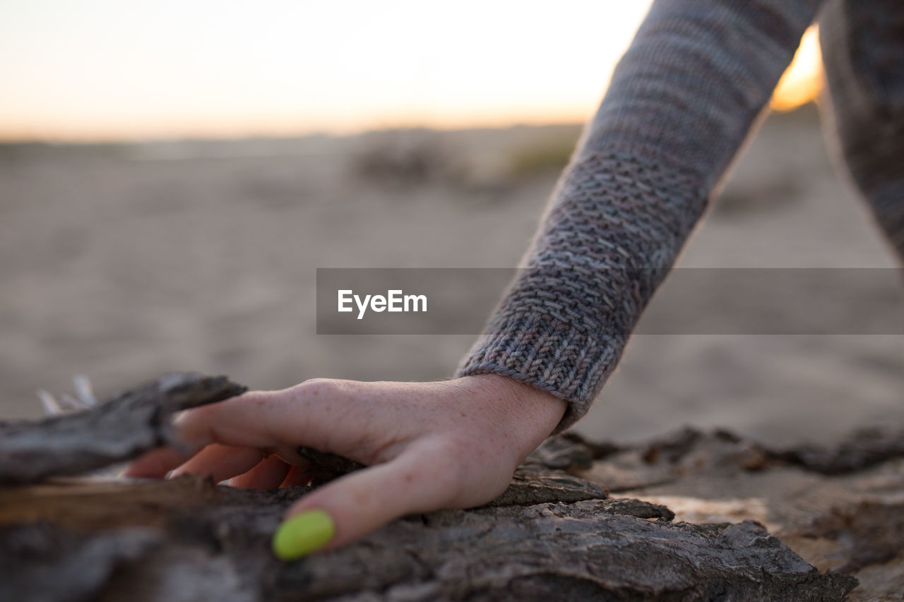 Cropped hand of woman on rock during sunset