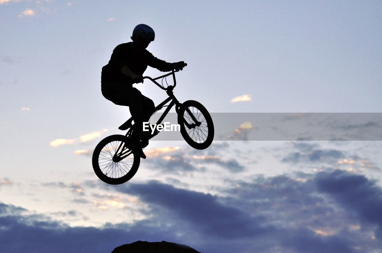 Low angle view of silhouette man riding bicycle against sky