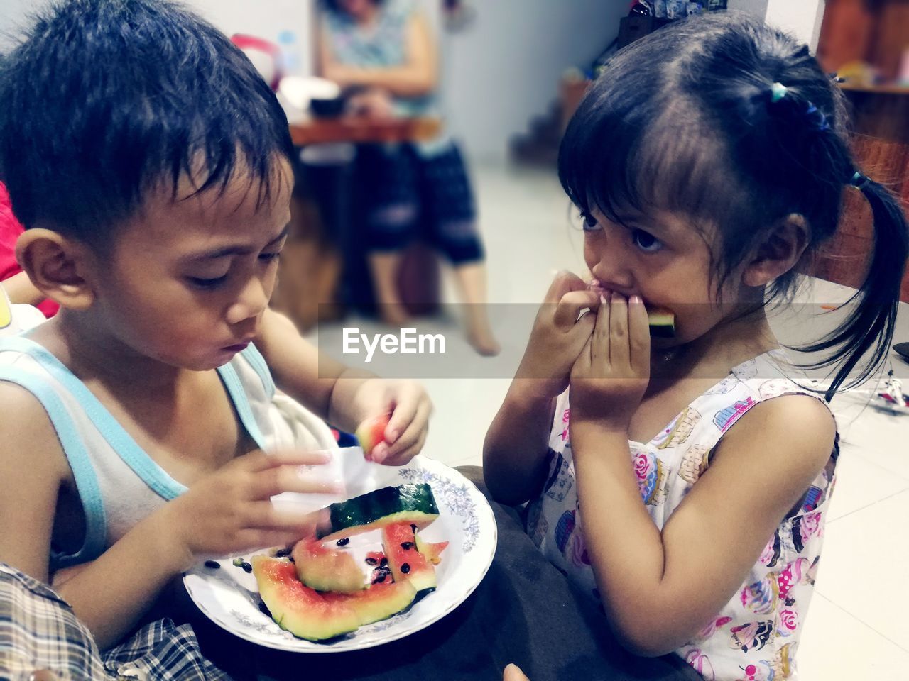 Close-up of siblings eating watermelon in plate at home