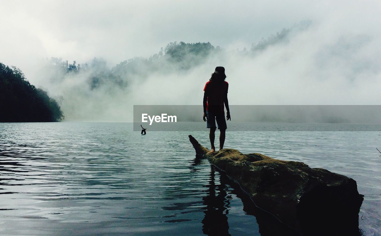 Man standing on log over ranu kumbolo lake during foggy weather