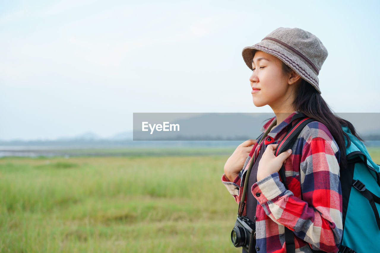 YOUNG WOMAN LOOKING AWAY WHILE STANDING ON LAND