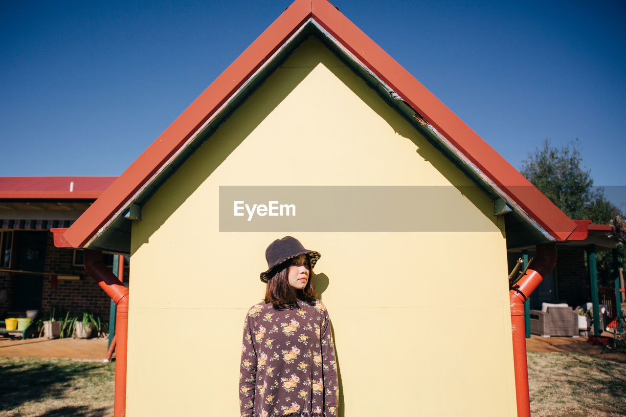 PORTRAIT OF WOMAN STANDING BY BUILDING