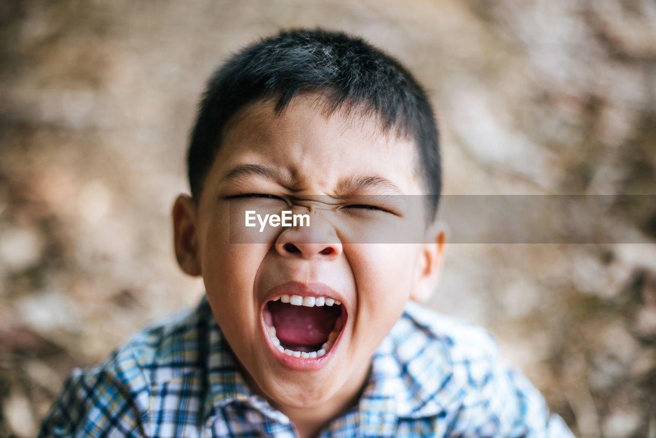 Close-up portrait of cute boy yawning while standing outdoors