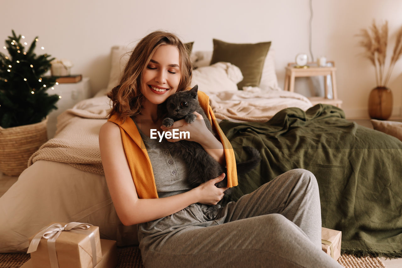 A pretty girl in pajamas rejoices and smiles during the christmas holidays in cozy bedroom interior