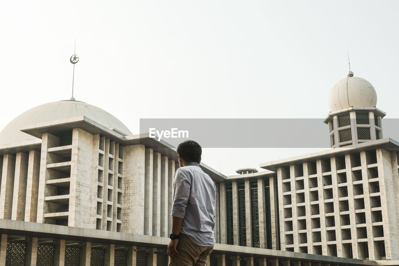 REAR VIEW OF MAN STANDING AGAINST BUILDINGS