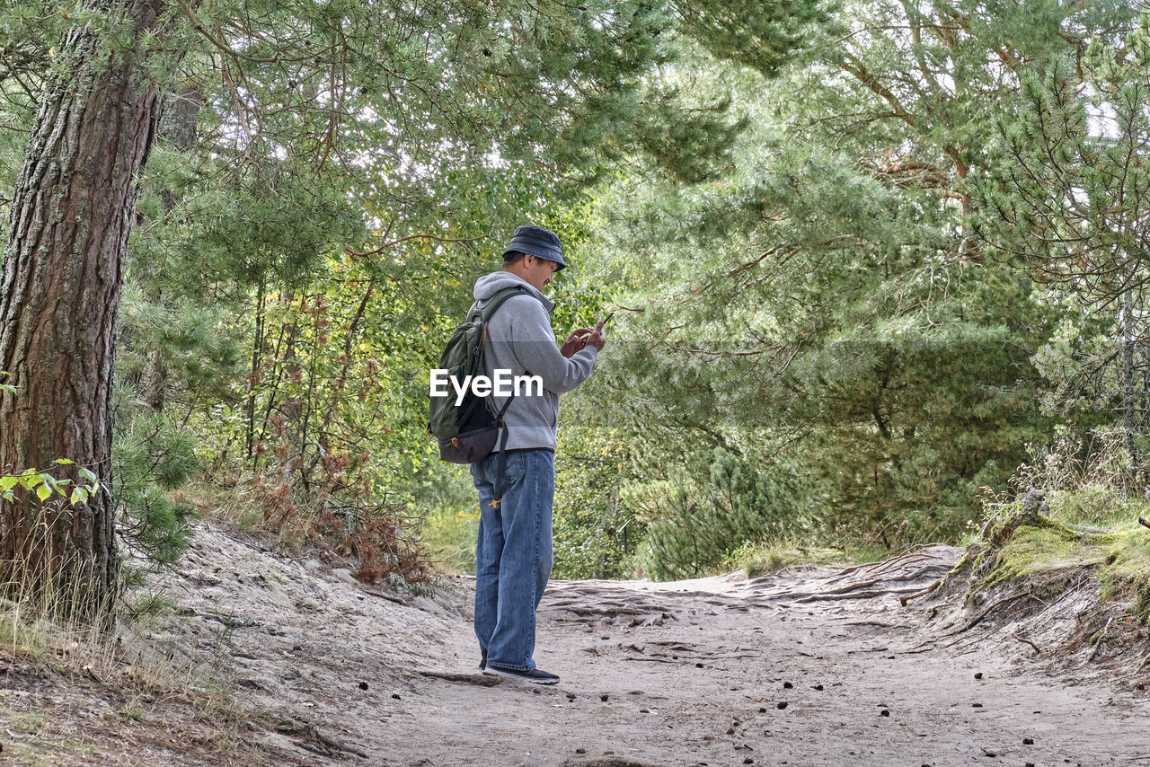 Side view of man standing and using phone in forest