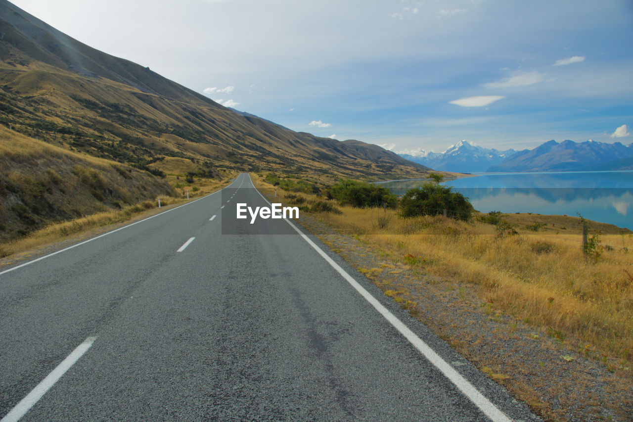 Empty road passing through mountain and lake