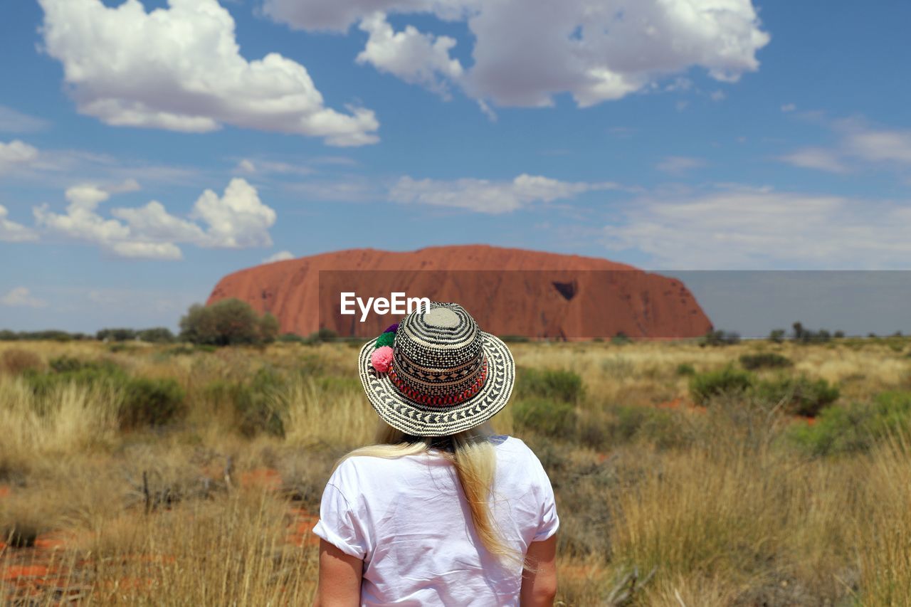 Rear view of woman in hat standing on field against sky