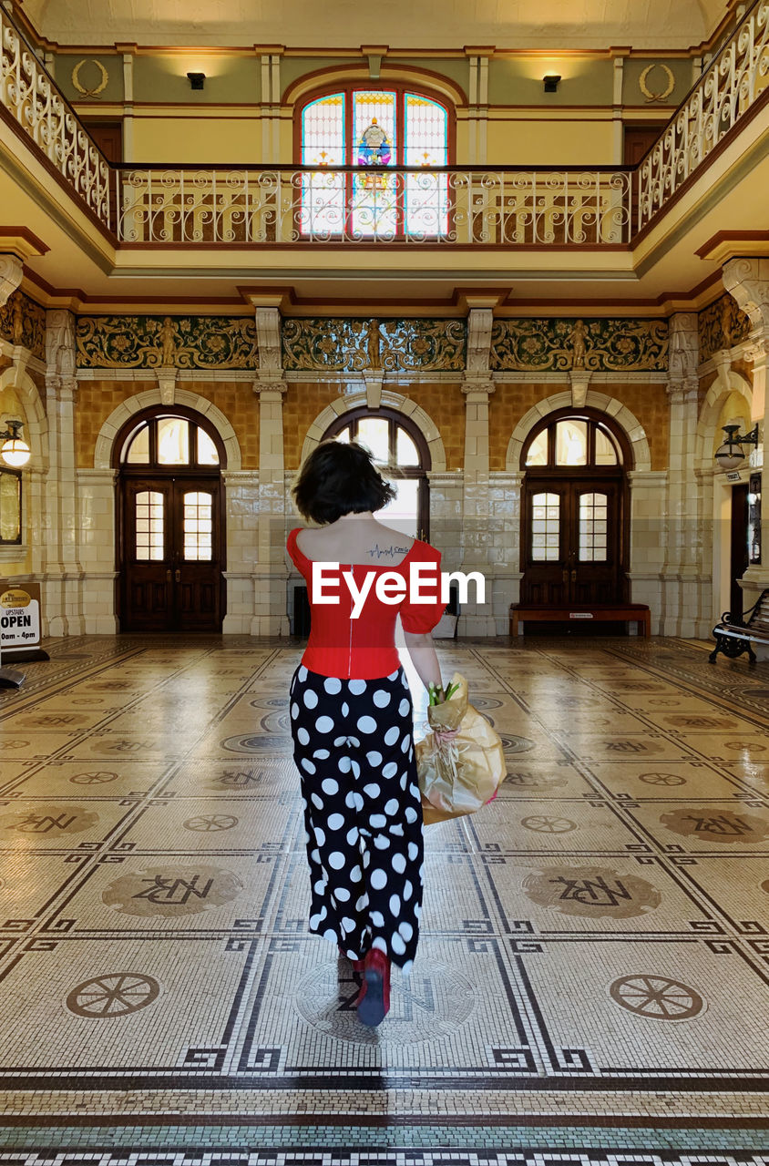 REAR VIEW OF WOMAN STANDING IN CORRIDOR