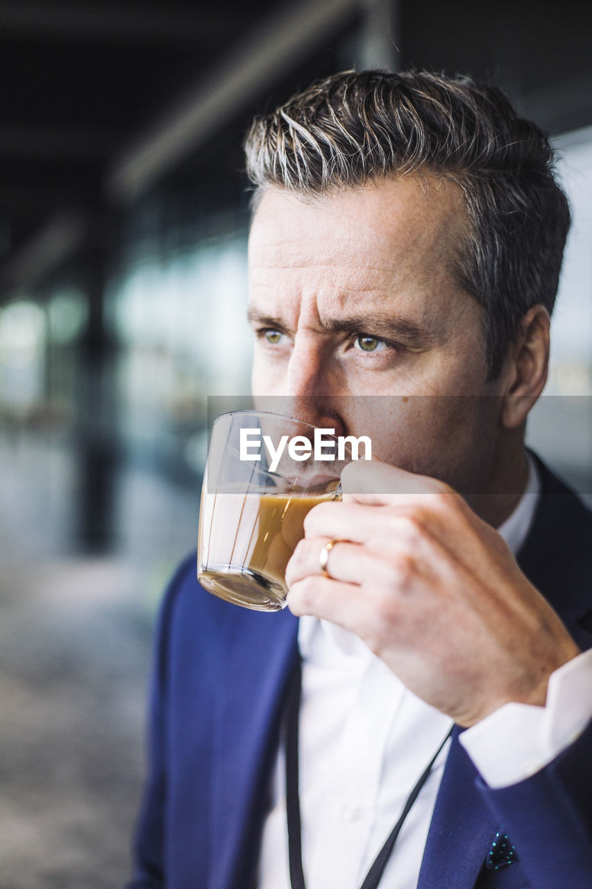 Businessman drinking tea while looking away at workplace