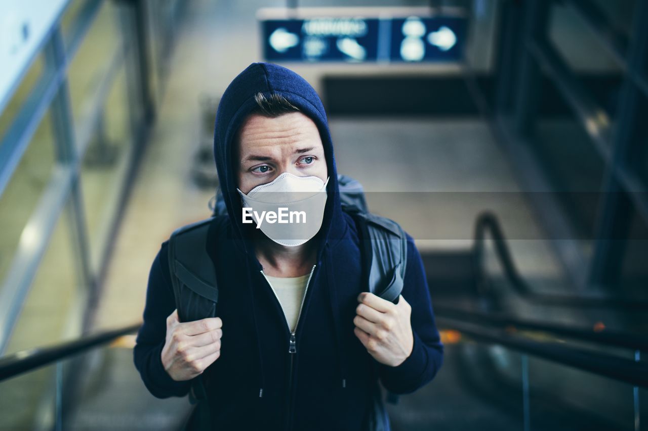 Man wearing mask looking away while standing on escalator at airport