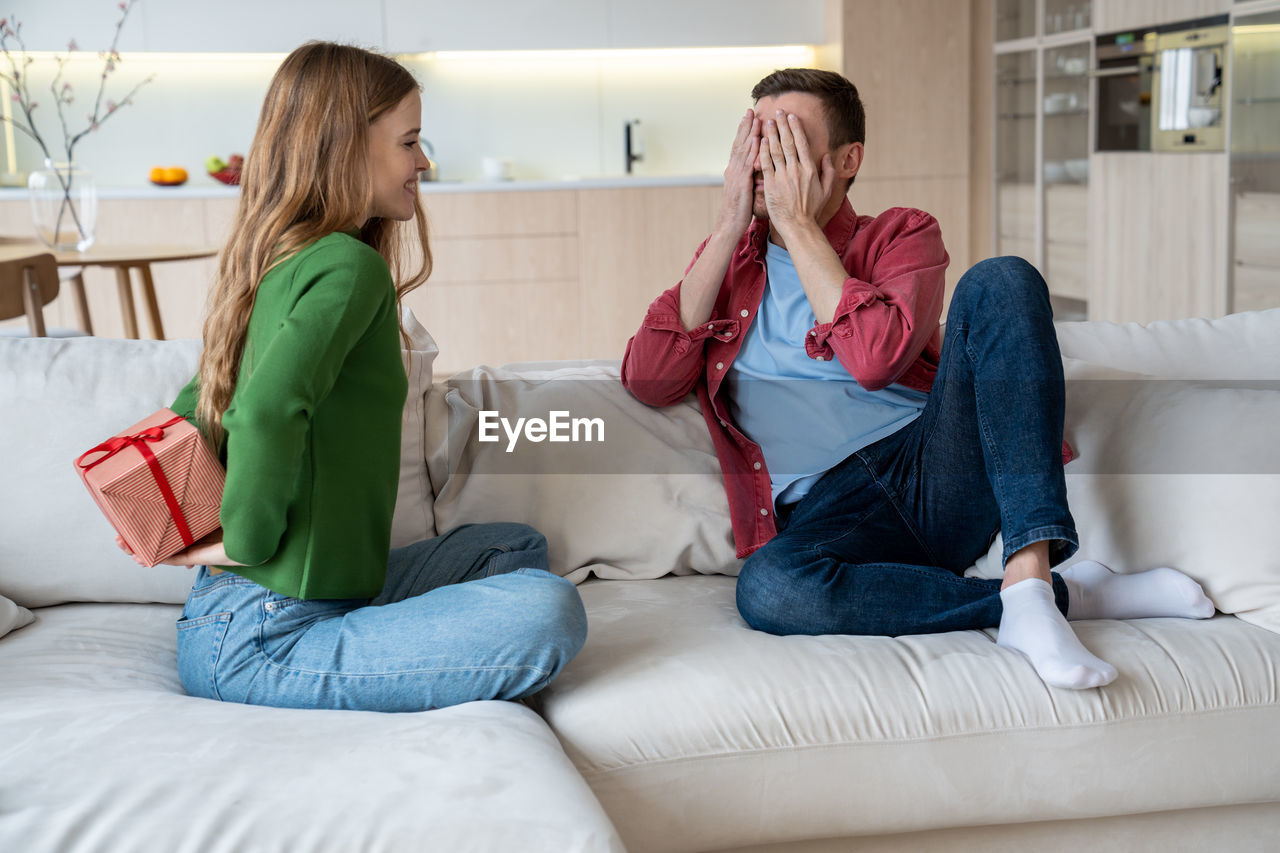 young woman using phone while lying on sofa at home