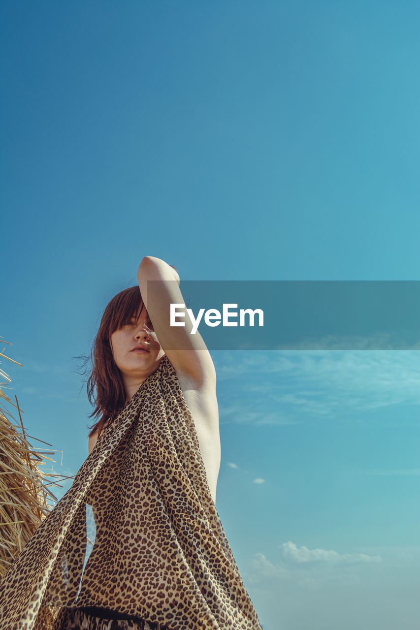 Low angle view of woman standing against clear blue sky