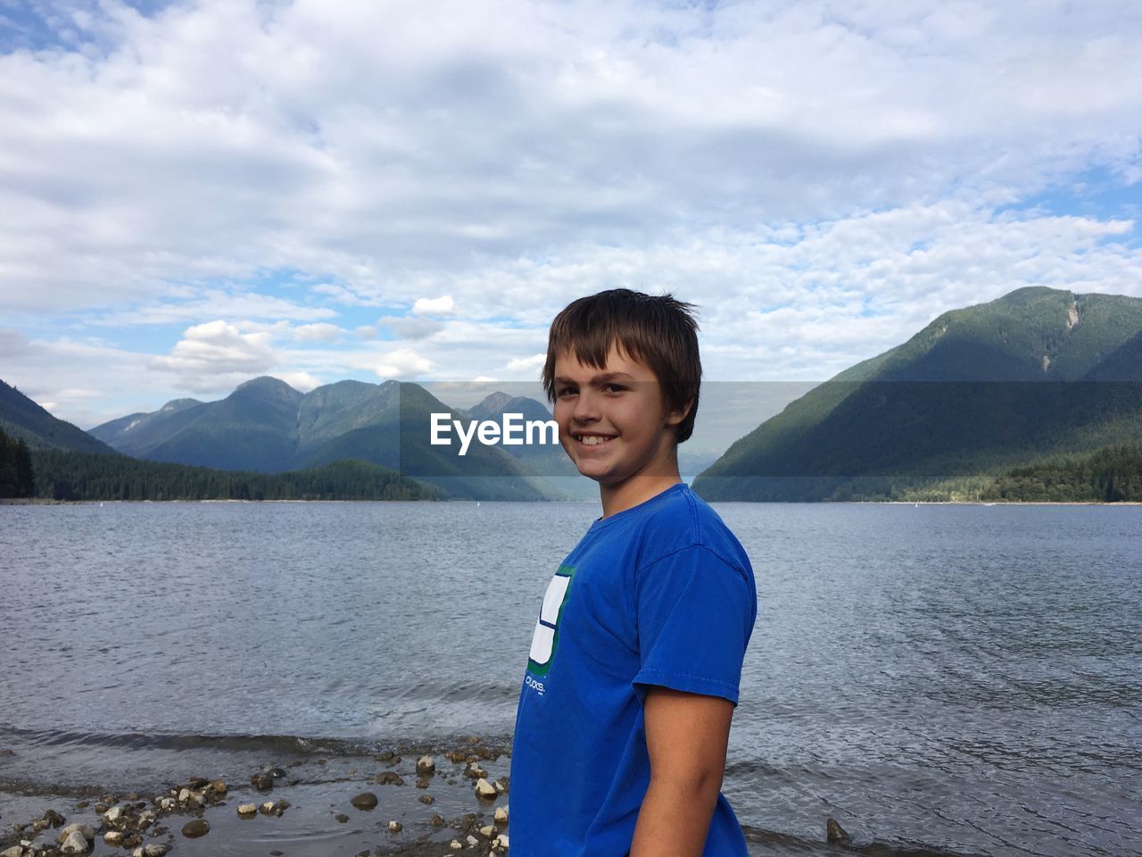 Portrait of smiling boy standing by lake against sky
