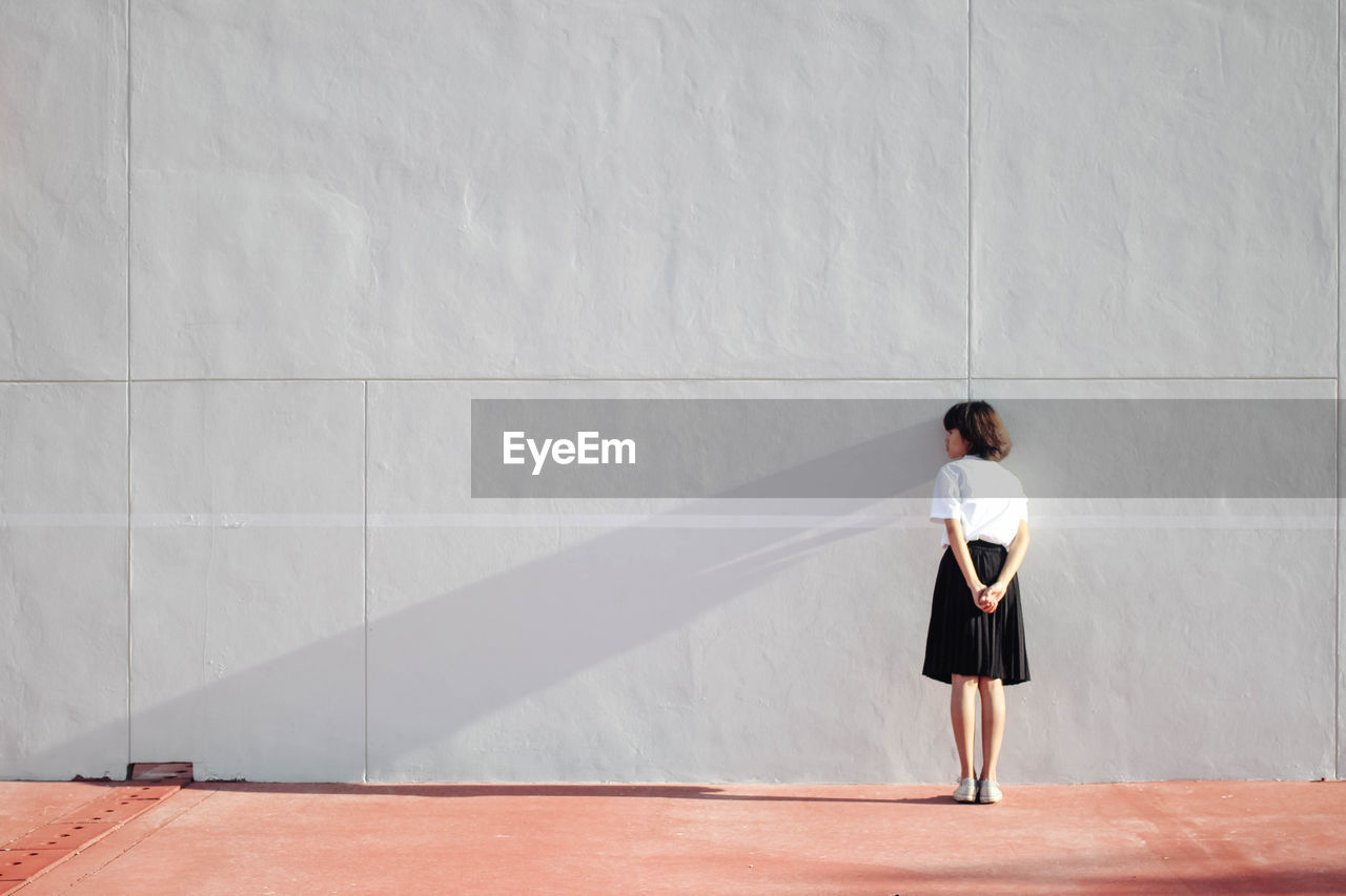 Rear view of young woman standing against wall