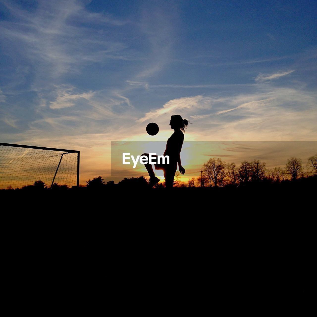 Silhouette woman playing soccer on field at sunset