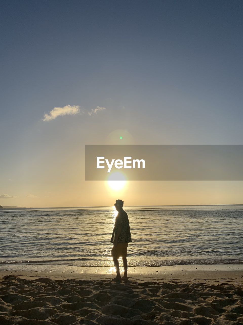 REAR VIEW OF WOMAN STANDING ON BEACH AGAINST SKY DURING SUNSET