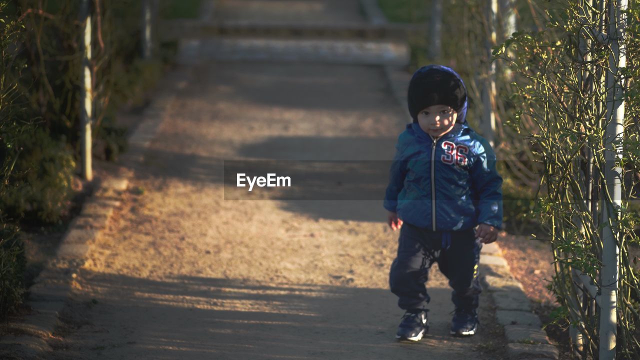 FULL LENGTH PORTRAIT OF SMILING BOY STANDING BY TREES