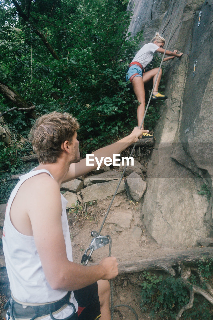 Man holding cable by woman climbing on rock formation