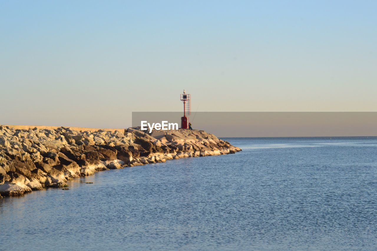 Lighthouse by sea against clear sky