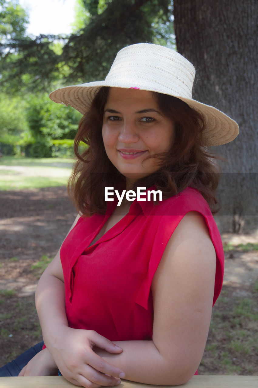 Portrait of smiling woman in hat standing against trees