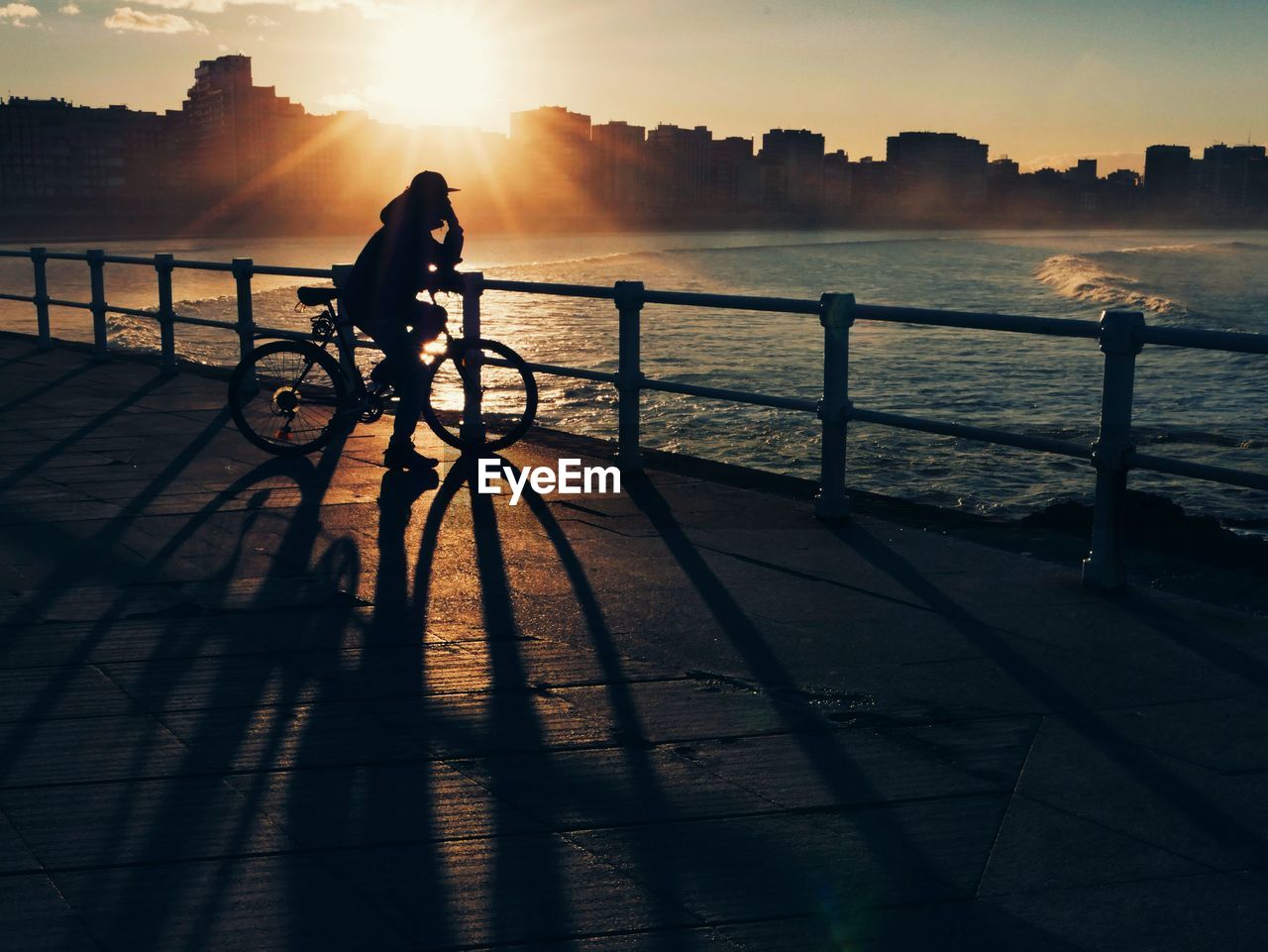 Silhouette person riding bicycle on promenade against sky during sunset