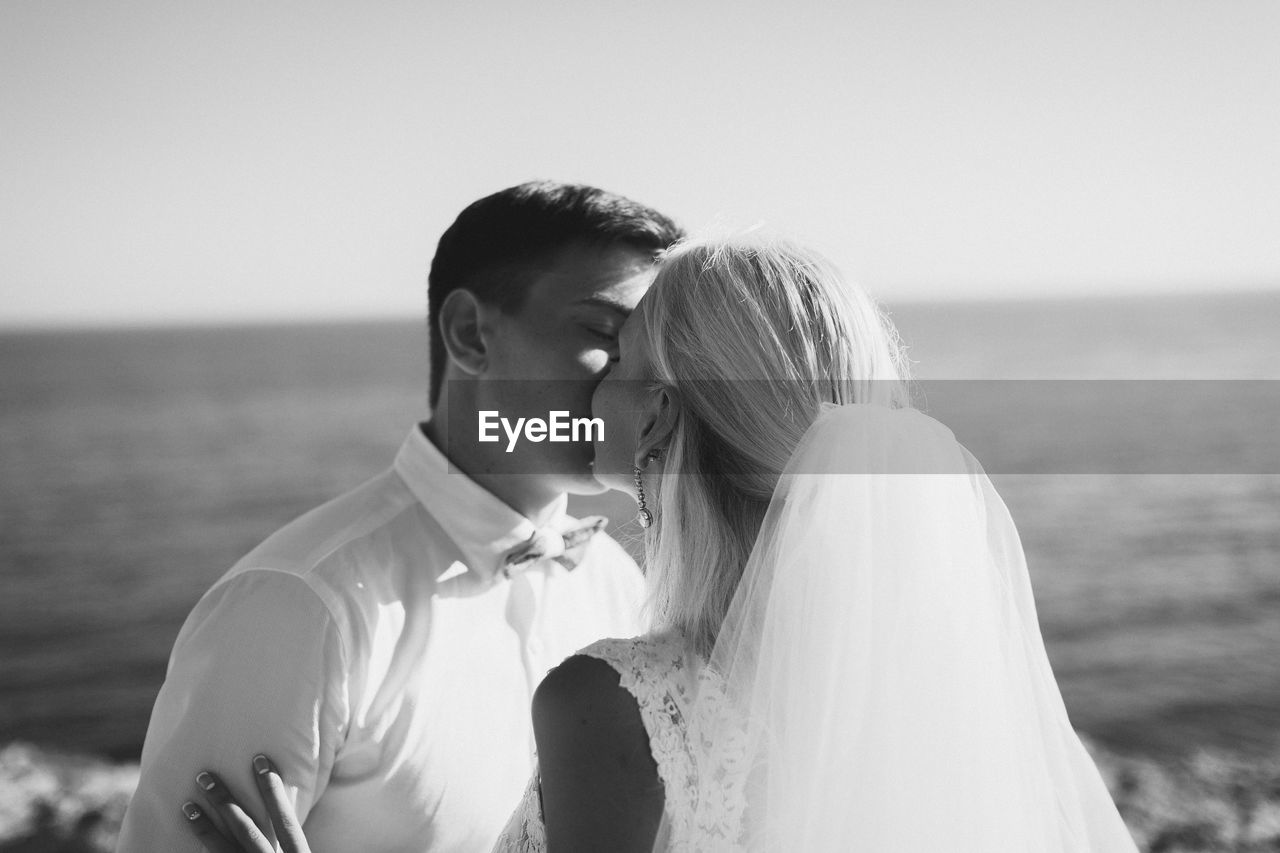 Bride and groom kissing against clear sky