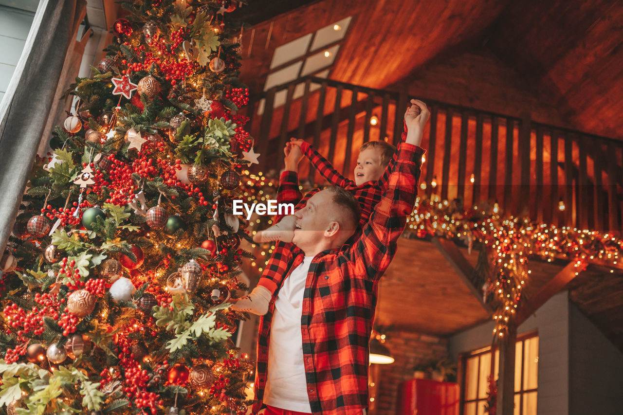 Candid authentic happy dad and son in red plaid pajamas fooling around at wood lodge xmas decorated
