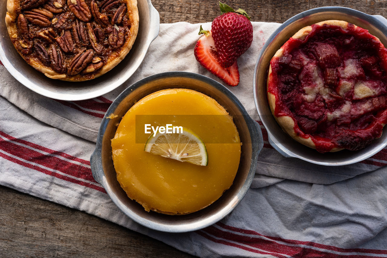 Above artisan baked lemon custard tart, pecan tart, and strawberry tart on retro style kitchen towel