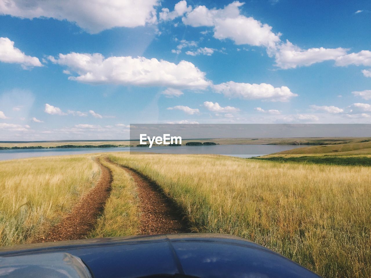 Cropped image of car on grassy field by lake against sky