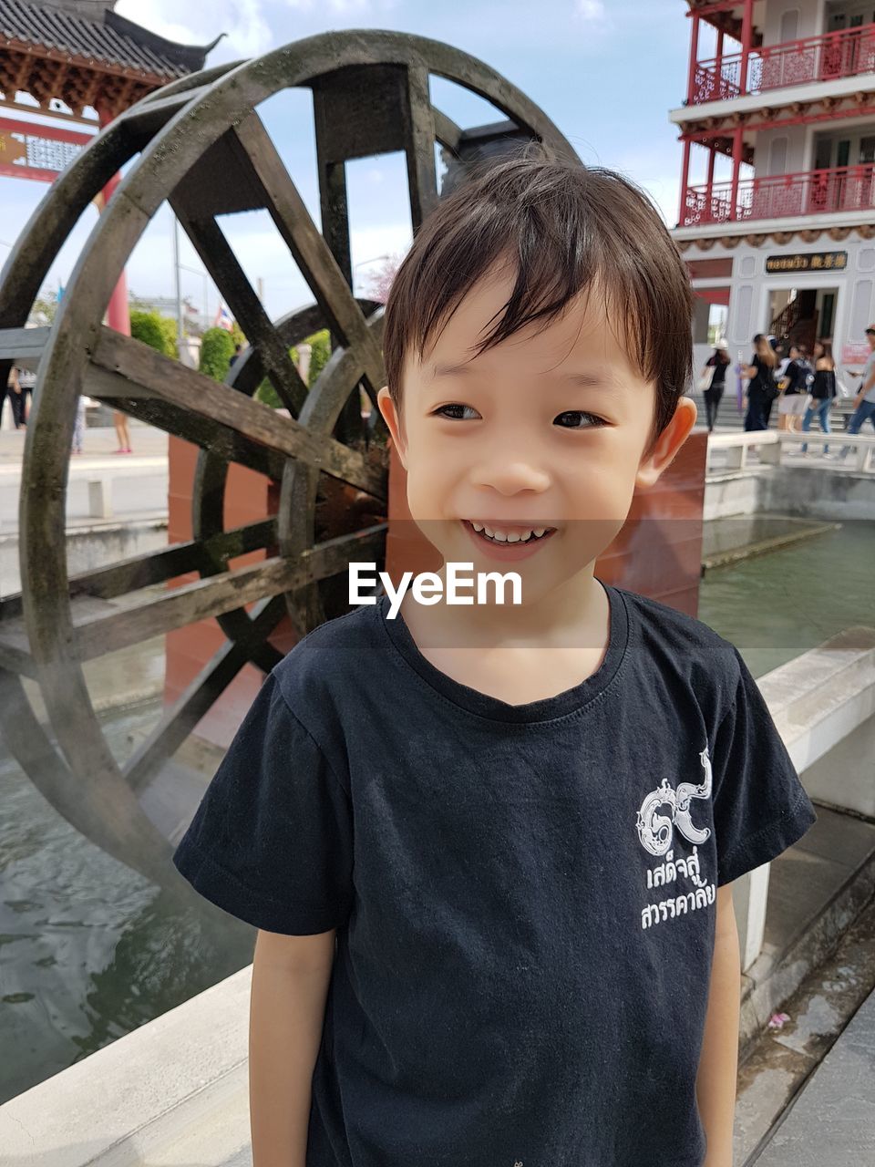 Thoughtful boy smiling while standing against watermill in pond