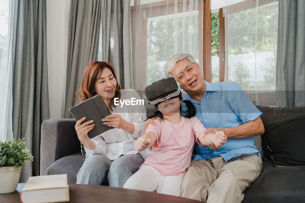 Grandparents sitting with granddaughter looking through virtual reality simulator at home