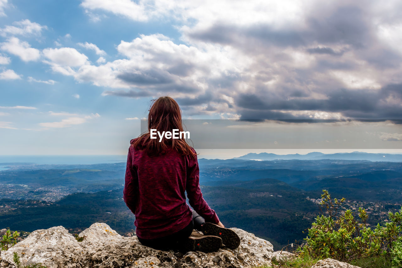 Rear view of woman sitting on rock against sky