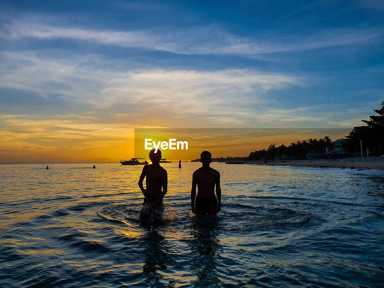 SILHOUETTE MEN ON SHORE AGAINST SKY DURING SUNSET