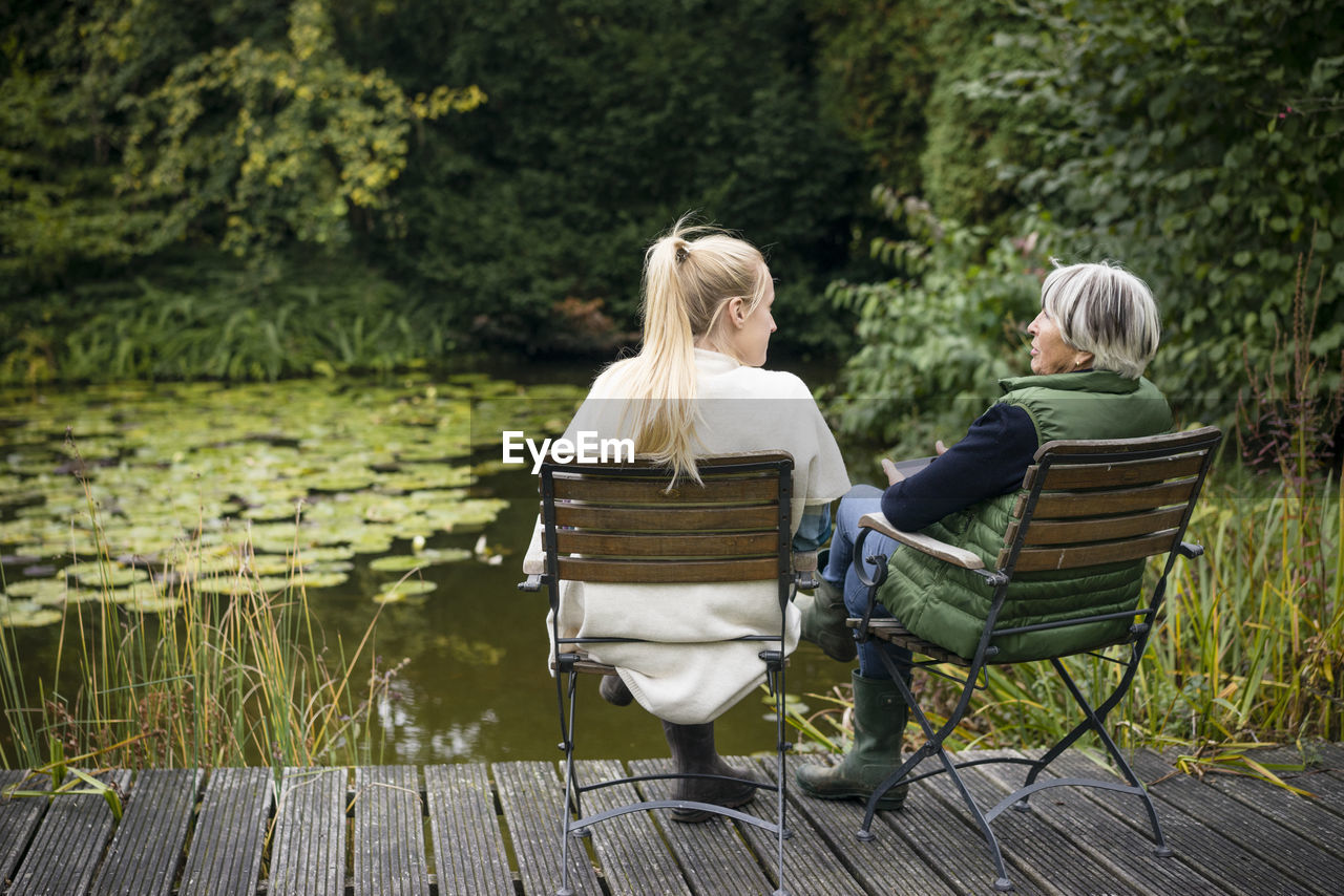 Young woman with her grandmother sitting on jetty at garden pond