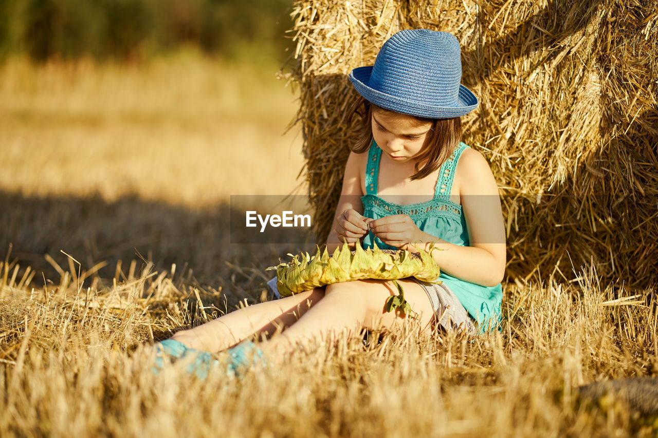 Happy girl sitting by hay on field