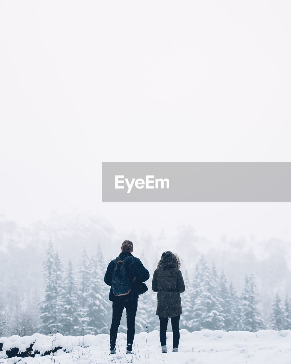 Rear view of man and woman standing on snow covered landscape