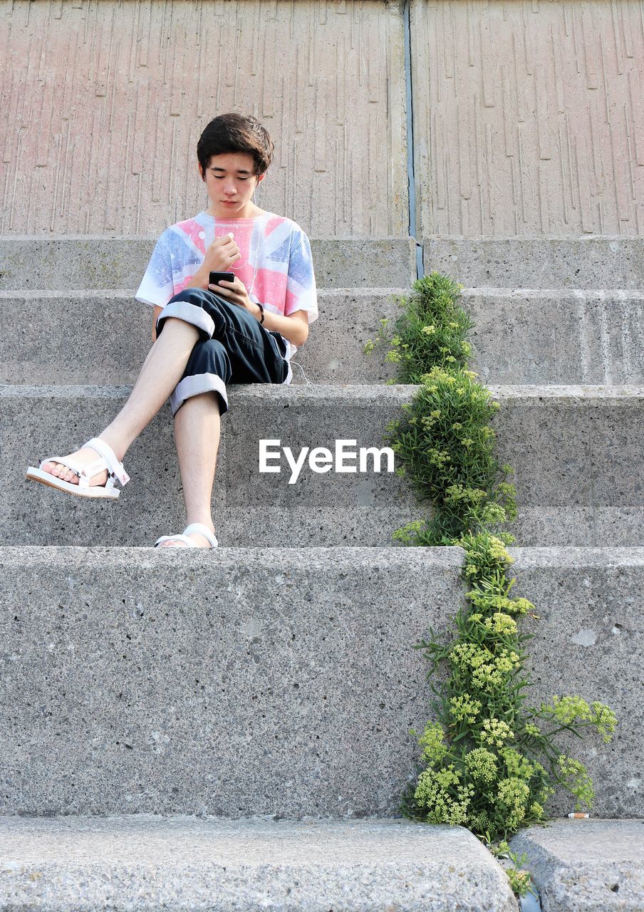 Full length of teenage boy using mobile phone while sitting on steps