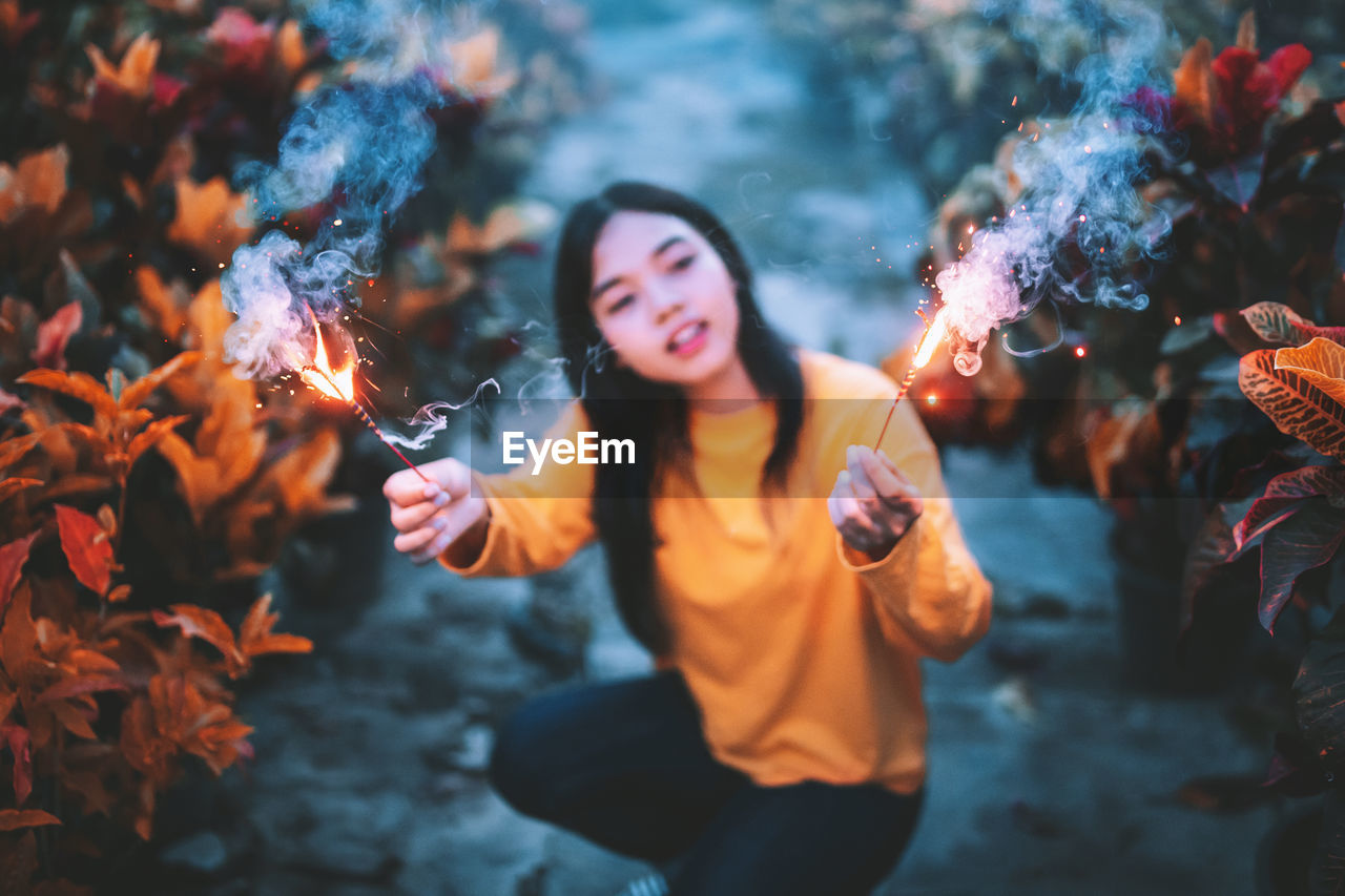 Young woman holding sparklers while crouching amidst plants