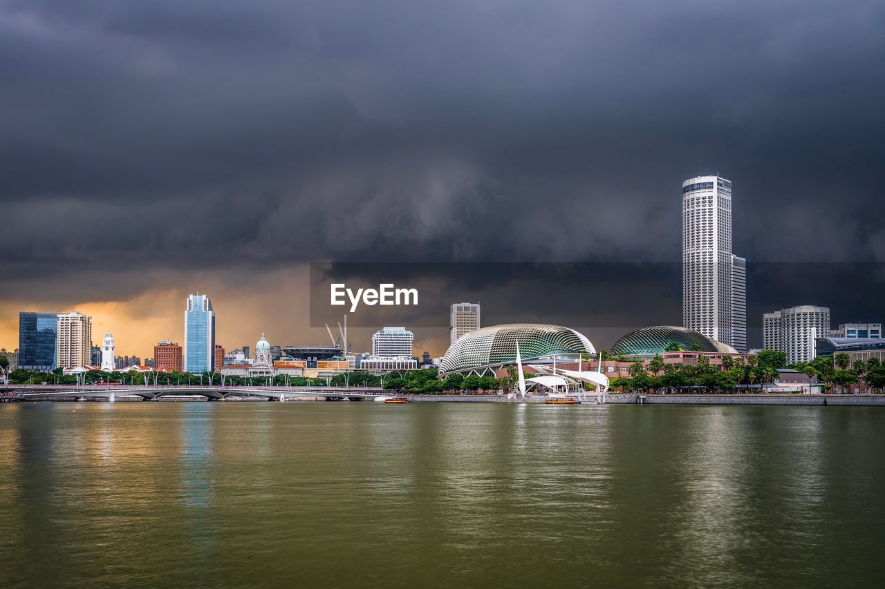 City at waterfront against cloudy sky