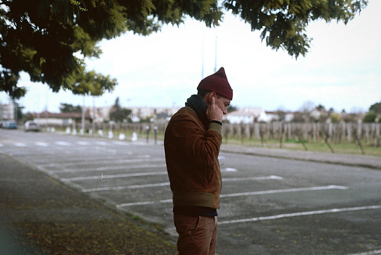 Side view of man standing by road against sky