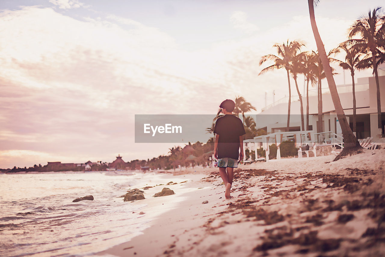 Pre teen boy walking on a tropical beach at sunset.