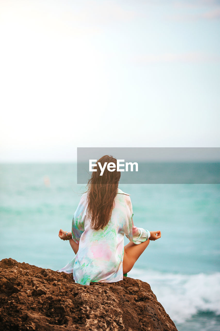 rear view of woman sitting at beach against clear sky during sunset