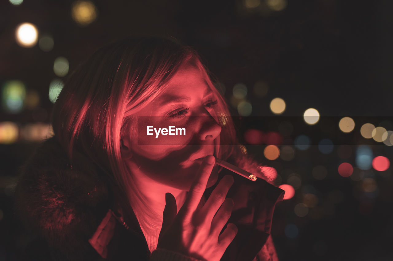 Close-up of young woman smoking cigarette at night