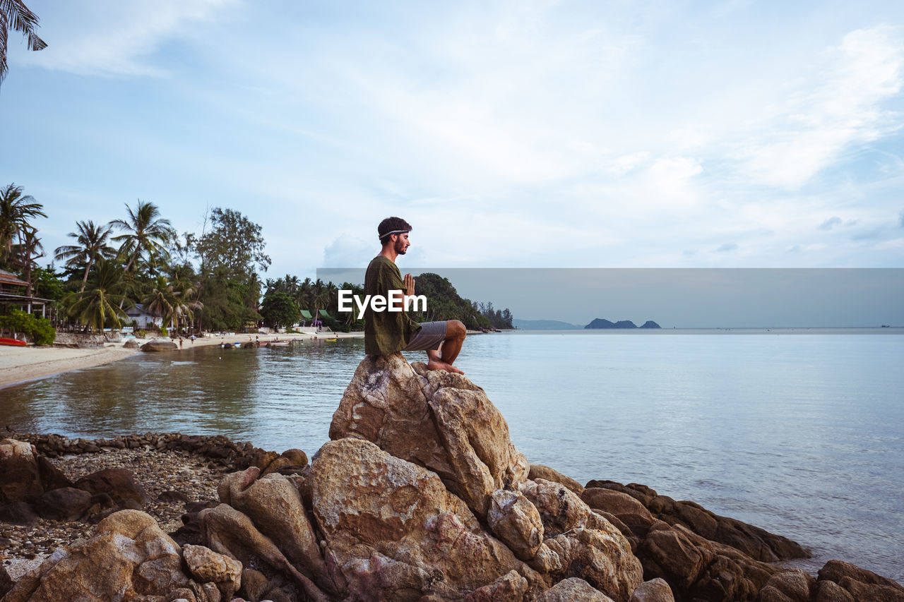 Man sitting on rock by sea against sky